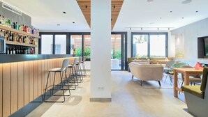 A modern bar area with stools, a counter with bottles, and a seating area with chairs and a table. - Sol y Miel Hostal (Benalmádena)