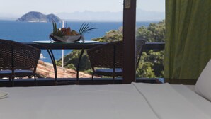 A balcony with wicker chairs, a table with a fruit bowl, and a view of the sea and mountains. - Colonna Galapagos Garden (Búzios)