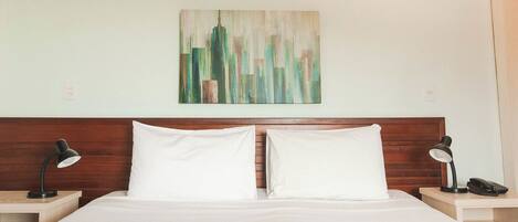 Een net opgemaakt bed met witte lakens, een houten hoofdbord en twee nachtkastjes met lampen en een telefoon.