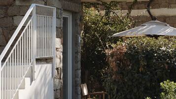 Un edificio in pietra con una scala bianca che conduce a una porta, una piccola zona esterna con una sedia e un giardino fiorito.