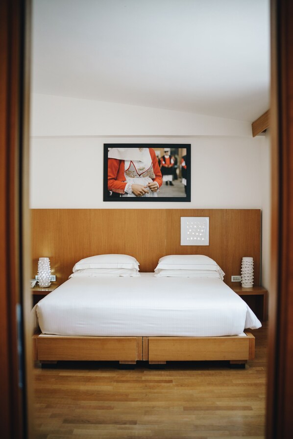 Una cama doble bien hecha con cabecera de madera, ropa de cama blanca y dos mesitas de noche con adornos.