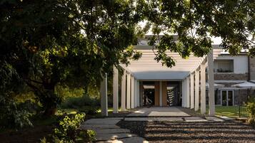 A pathway leading to a building with a covered entrance, surrounded by trees and greenery.