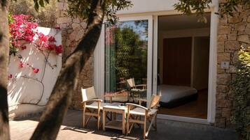 A cozy outdoor seating area with a table and chairs, a stone wall, and a bed visible through a glass door.