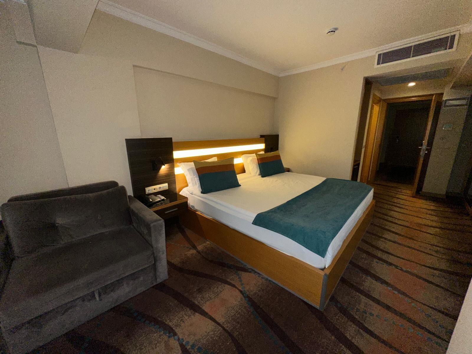 Una habitación de hotel con una cama, una mesita de noche, una lámpara y una silla.
