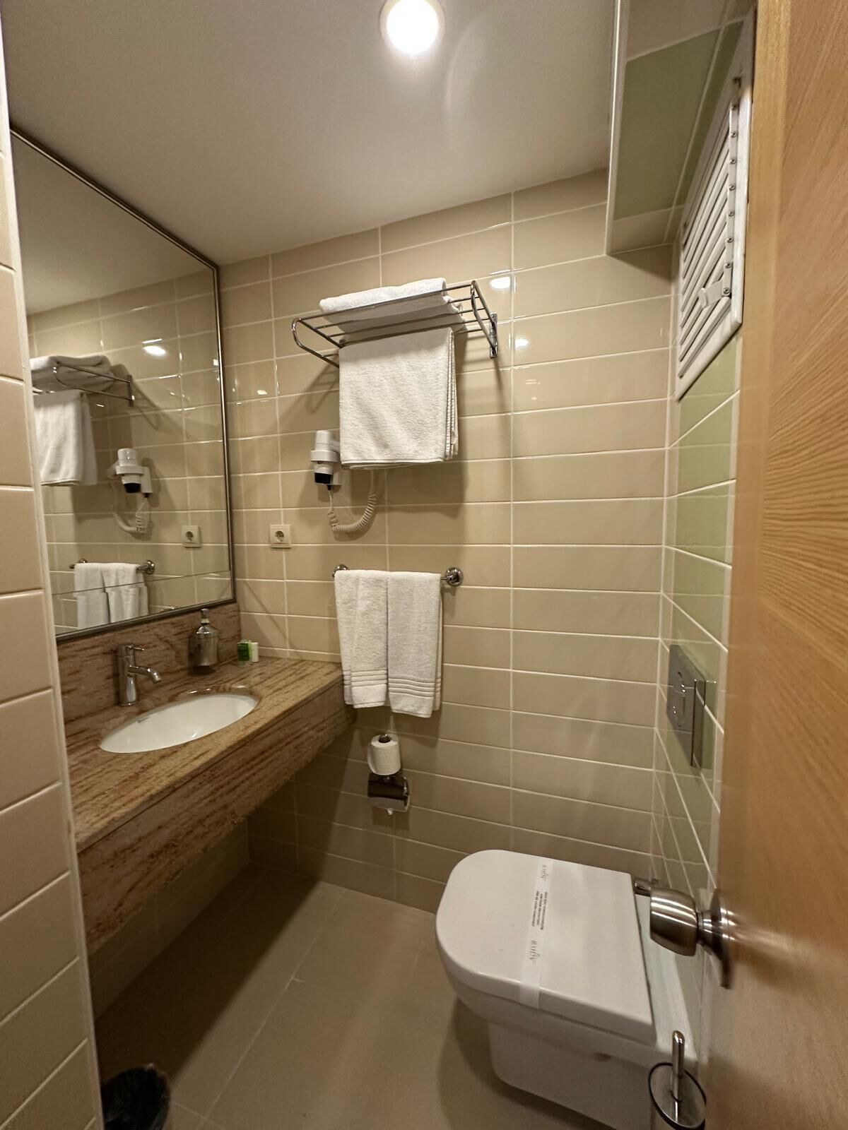 A compact bathroom with a sink, mirror, towel rack, and toilet.