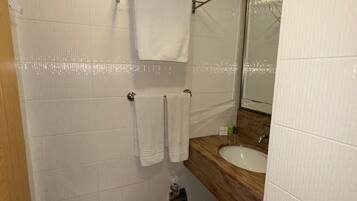 Un baño con inodoro blanco, tocador de madera con lavamanos y espejo. Hay dos toallas colgadas en un perchero.