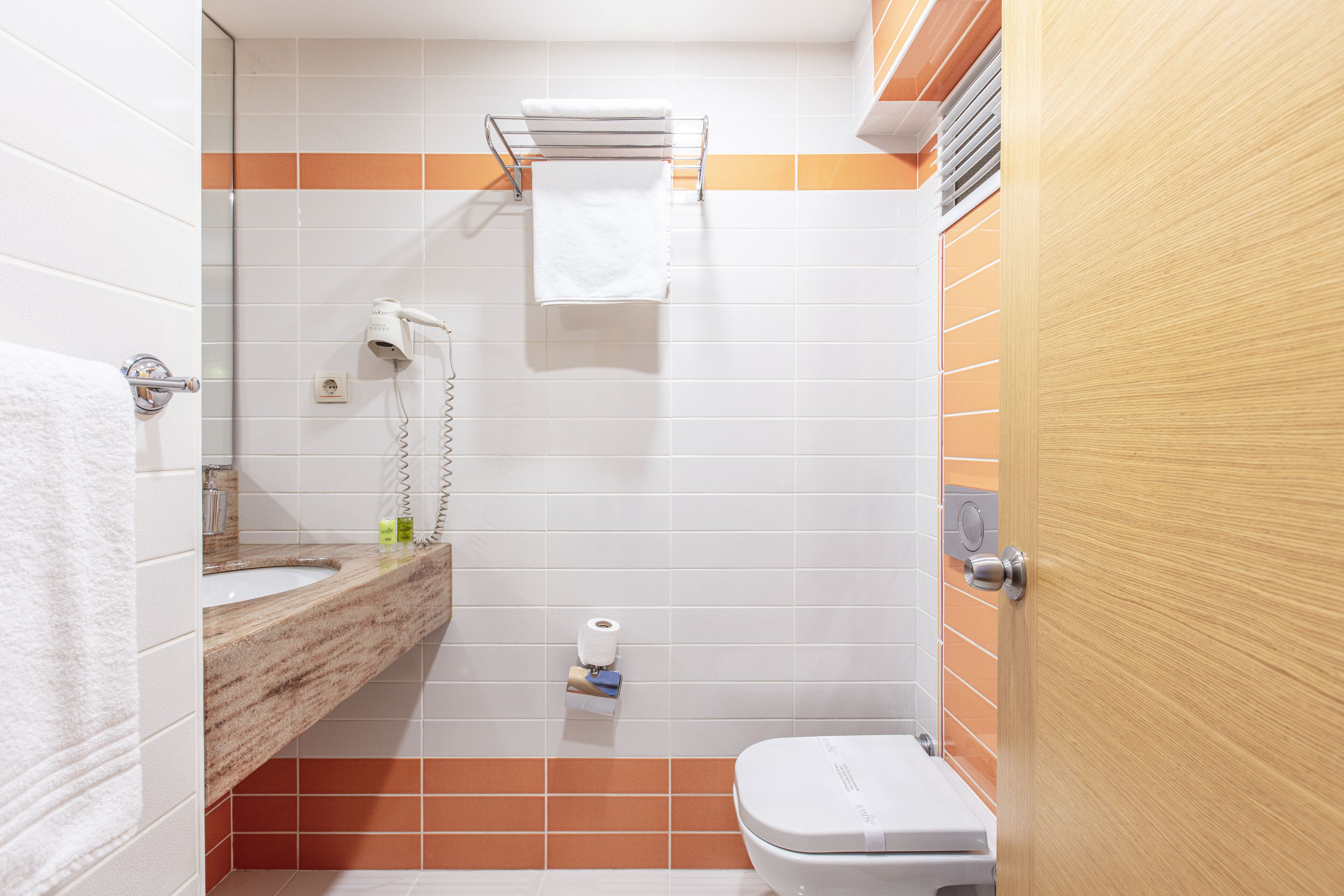 Un bagno con lavandino, specchio, portasciuga, water e soffione.