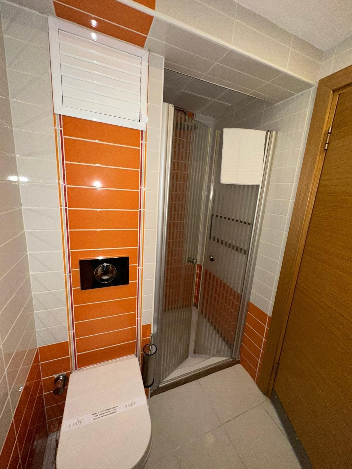 Un baño con inodoro blanco, ducha con puerta de cristal y paredes con azulejos naranja.