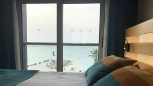 Una habitación de hotel con un gran ventanal que da a una playa y al mar.