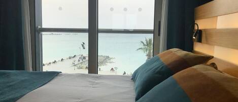 A hotel room with a large window overlooking a beach and the sea.