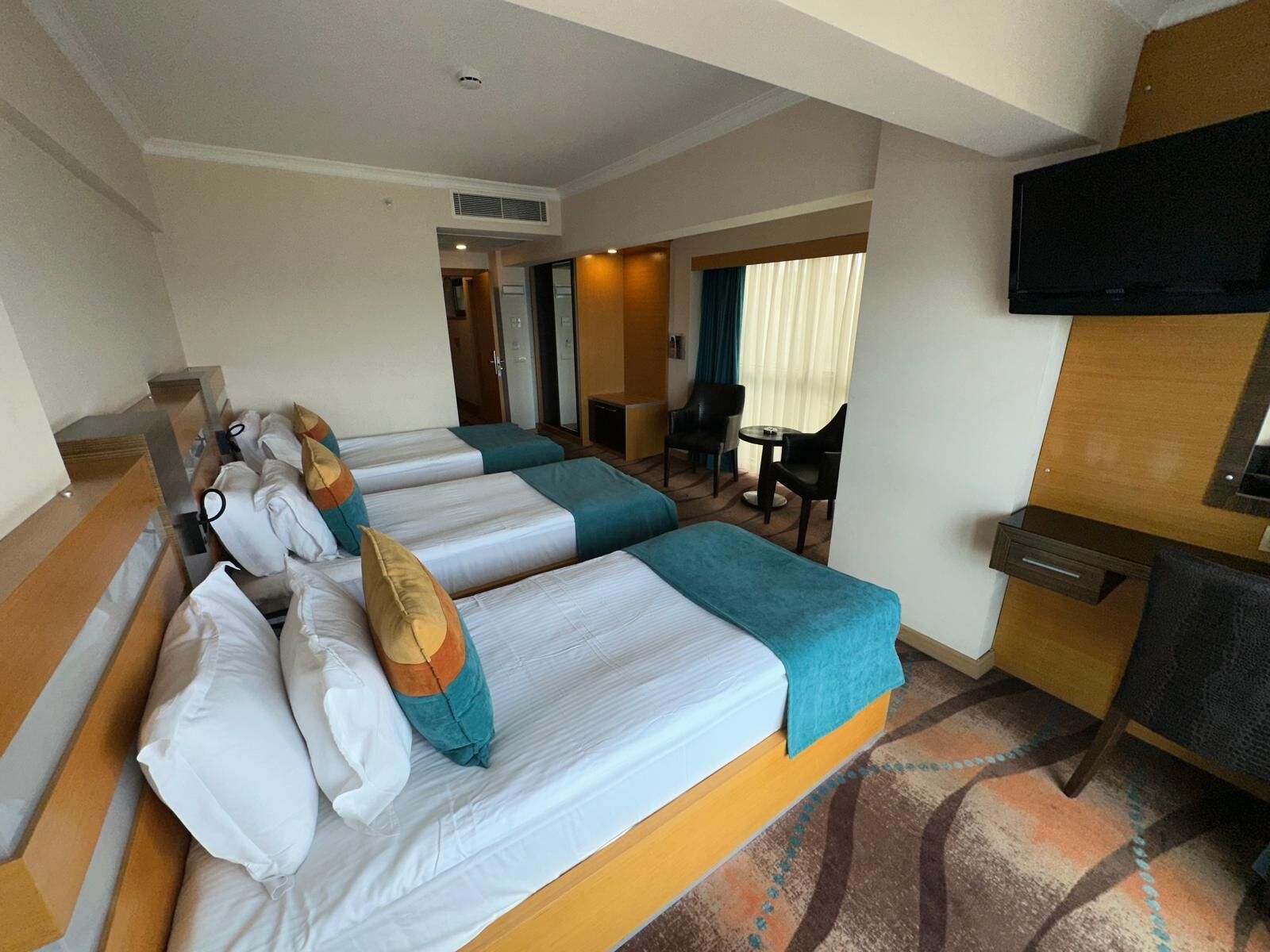 A hotel room with three beds, a TV, a desk, and a chair.