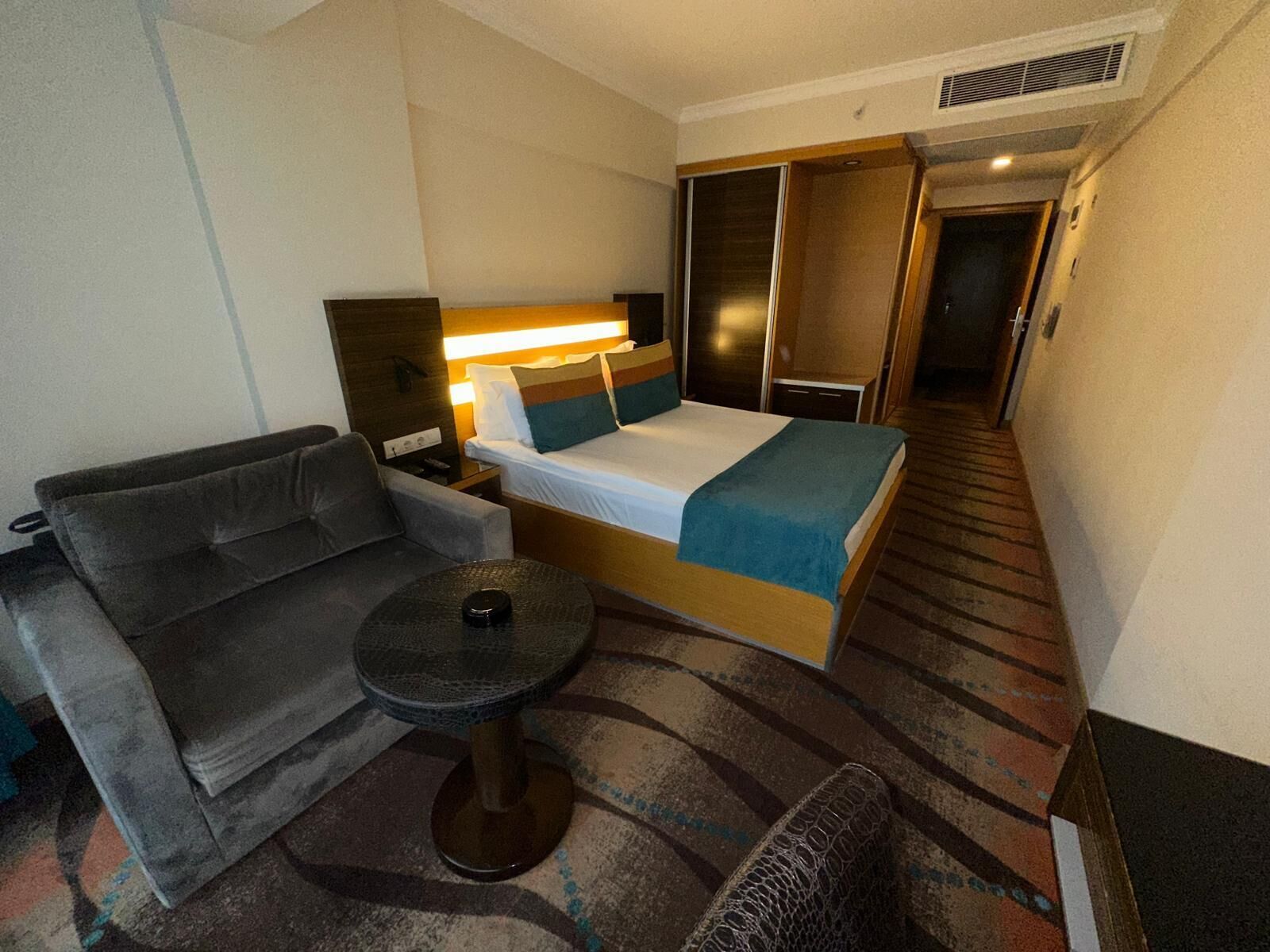 A hotel room with a bed, a sofa, a small table, and a wardrobe.