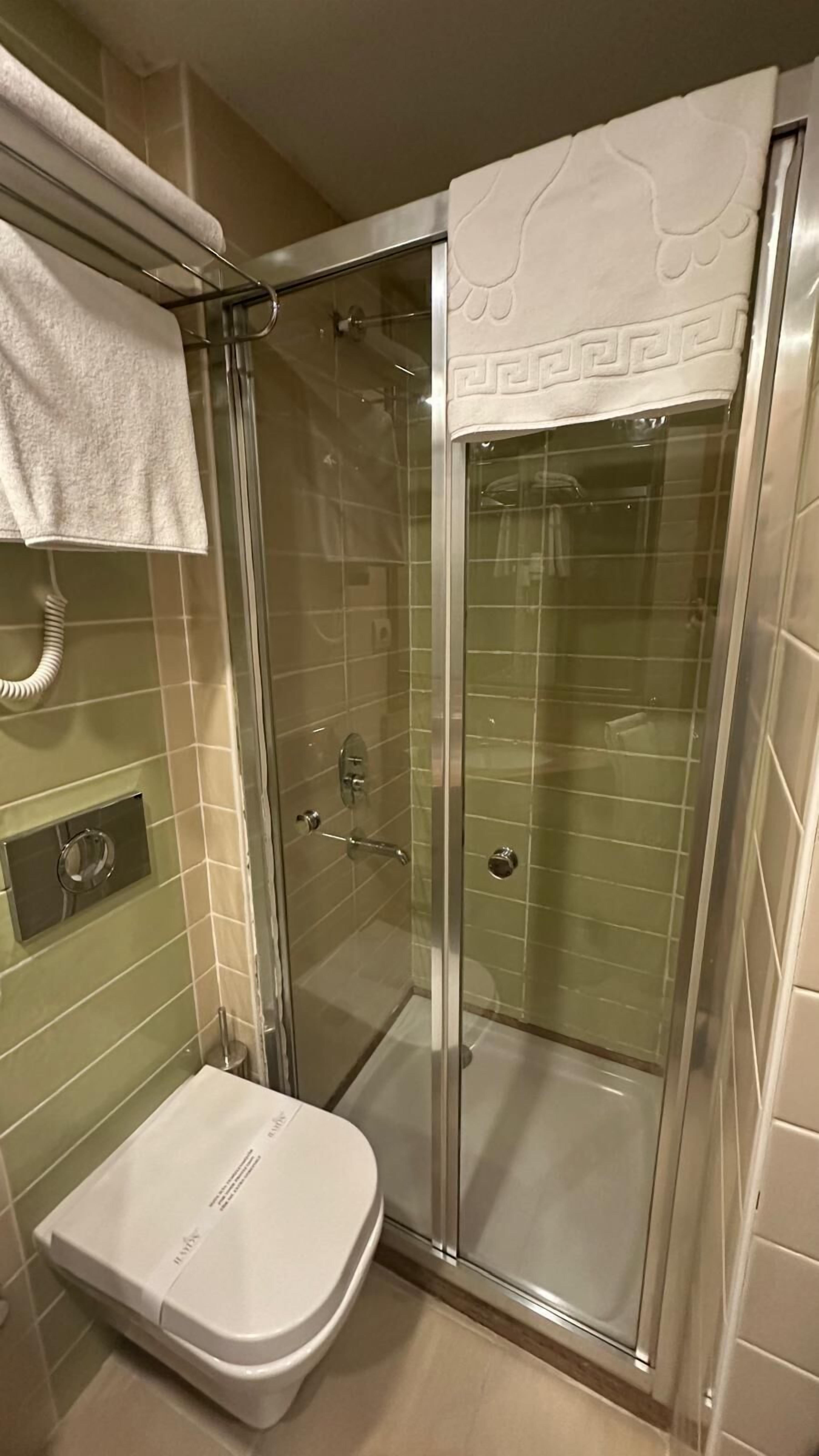 Cabina de ducha con paredes de vidrio, inodoro blanco y toallero arriba.