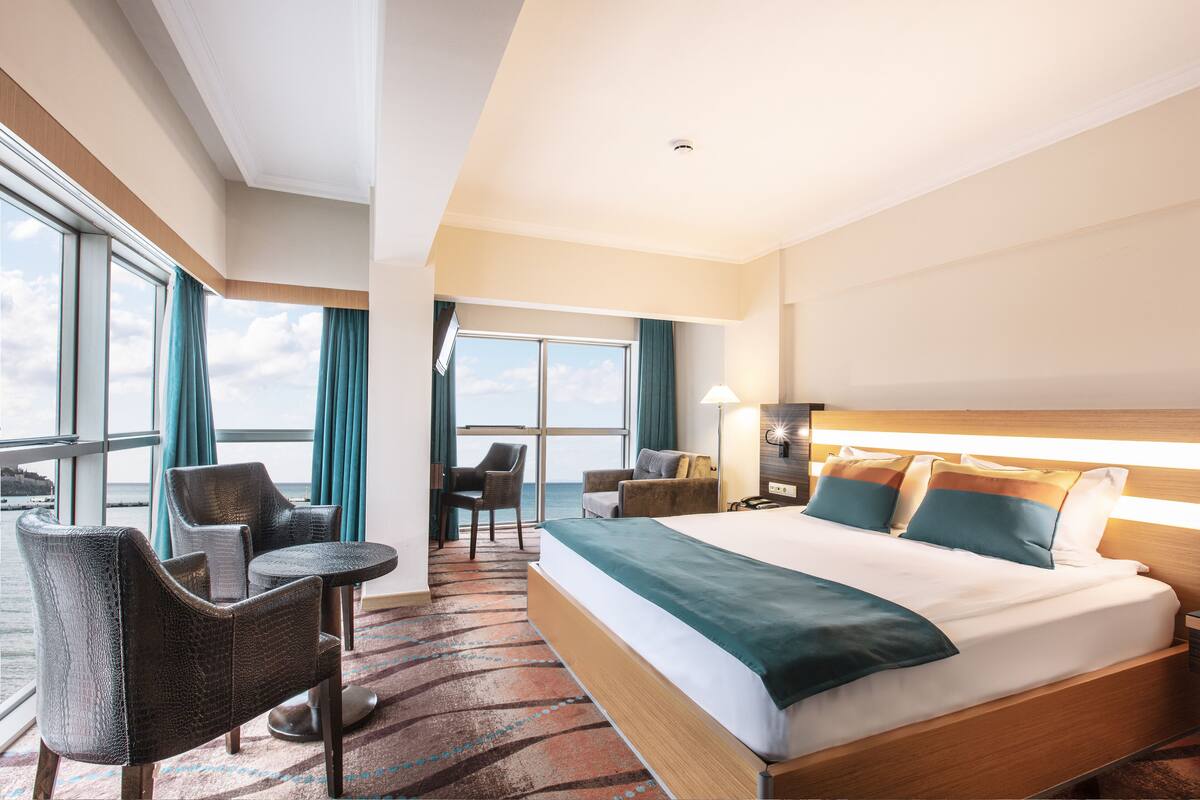 Ein Hotelzimmer mit einem großen Bett, zwei Sesseln, einem kleinen Tisch und Meerblick durch große Fenster.