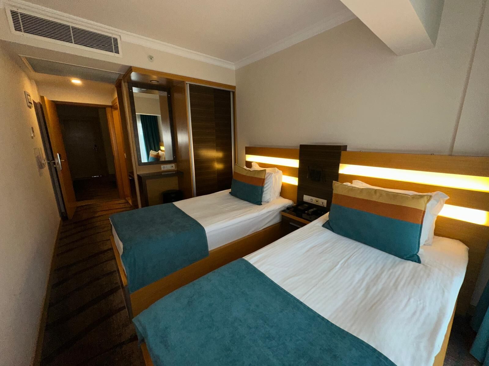 A hotel room with two beds, a mirror, a wardrobe, and a small table.