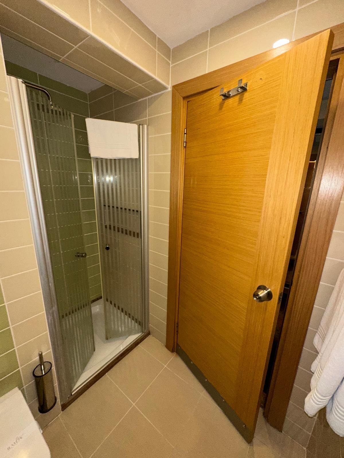Une salle de bain avec une douche à parois de verre, une porte en bois et une serviette blanche accrochée au mur.
