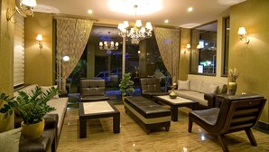 Un salón luminoso con sofá, sillones y una mesa de centro. Se observan cortinas, una araña y apliques de pared.