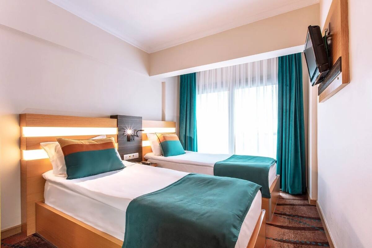 Ein Hotelzimmer mit zwei Betten, einem an der Wand befestigten Fernseher und einem Fenster mit Vorhängen.