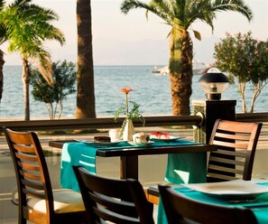 Une table recouverte d’une nappe turquoise, avec des chaises en bois et une petite plante en pot ornée d’une fleur rouge.
