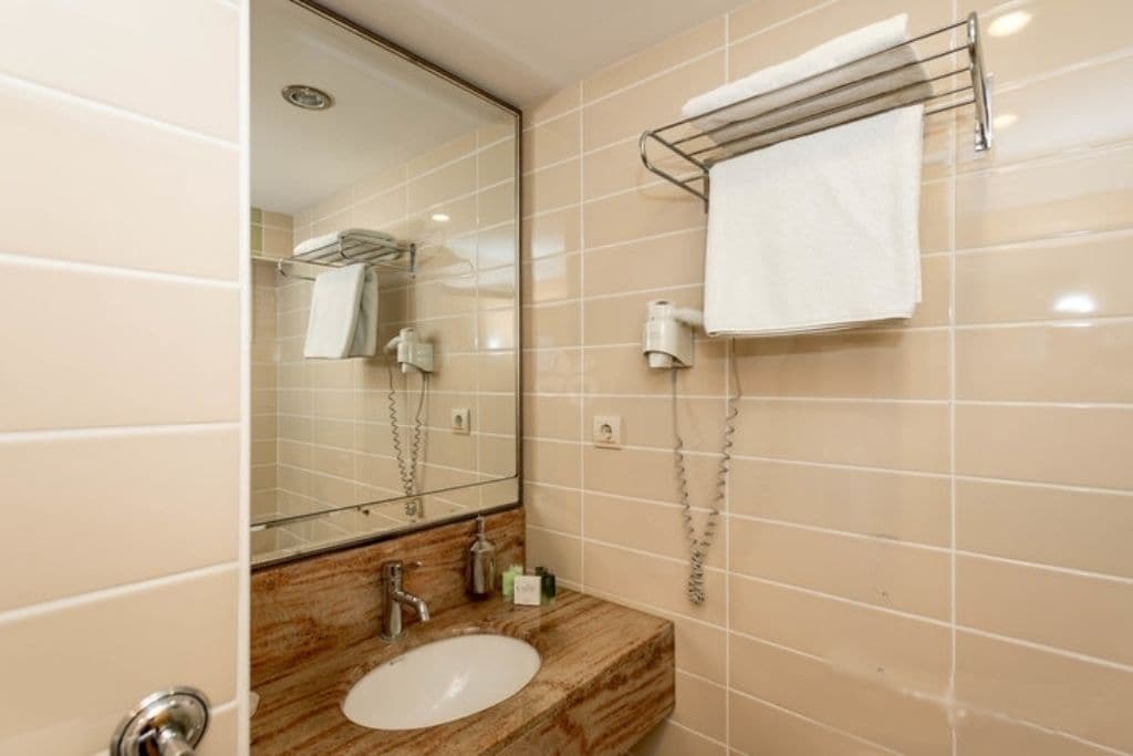 Een badkamer met een marmeren wastafel, een spiegel, een handdoekhouder en een douchehoek.