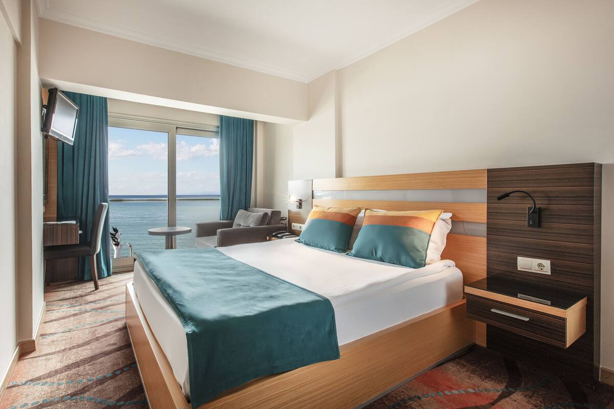 Ein Hotelzimmer mit einem großen Bett, einem Schreibtisch, einem Sessel, einem kleinen Tisch und Blick aufs Meer.