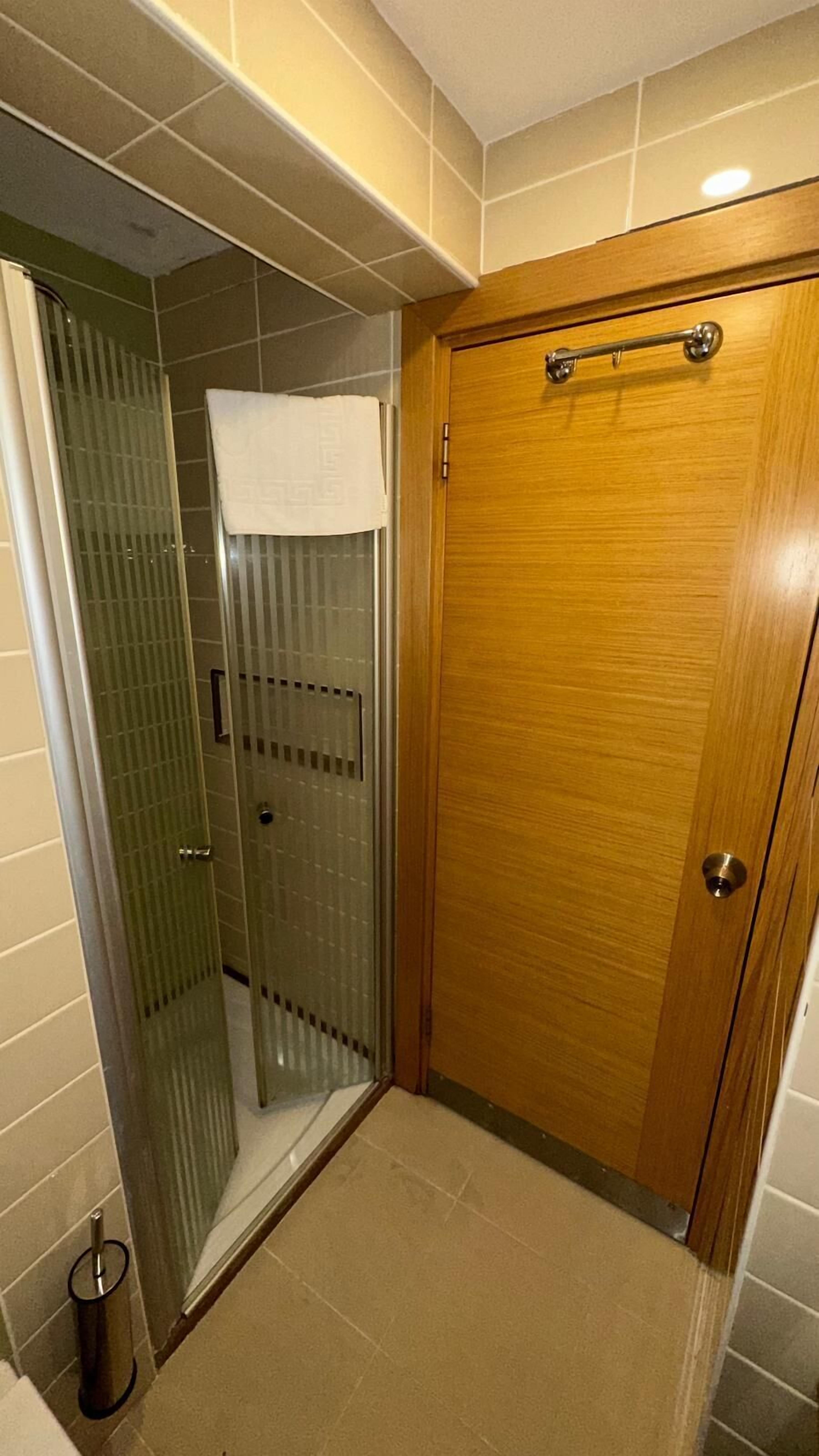 Un baño con cabina de ducha de vidrio, puerta de madera y una toalla colgada del pomo de la ducha.
