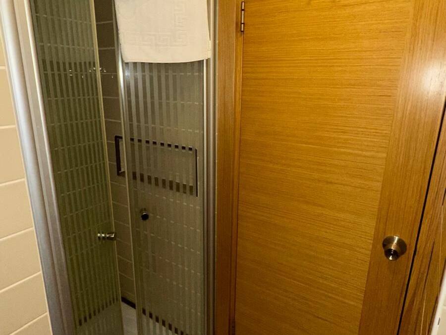 Un baño con cabina de ducha de vidrio, puerta de madera y una toalla colgada del pomo de la ducha.
