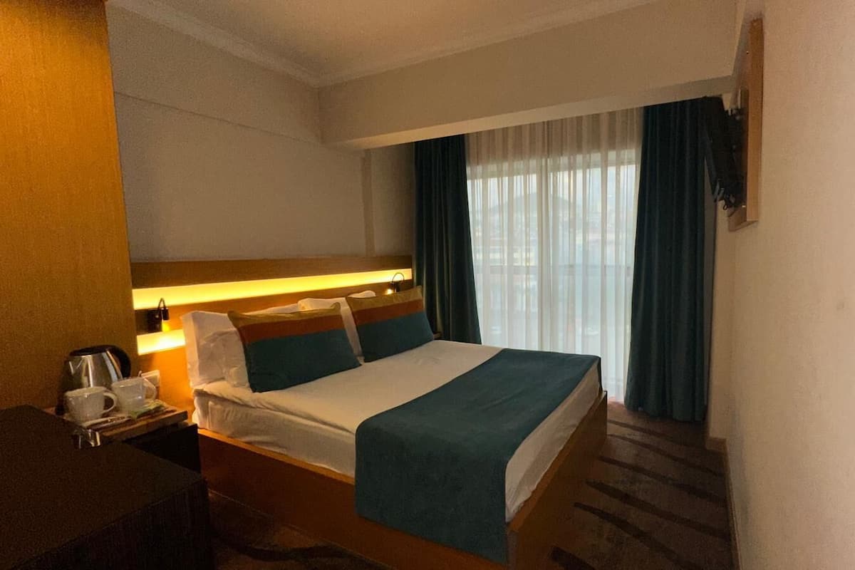 Ein Hotelzimmer mit Bett, Nachttisch und einem fenster mit Vorhängen.