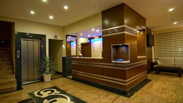 A reception area with a reception desk, a potted plant, an elevator, and a staircase.
