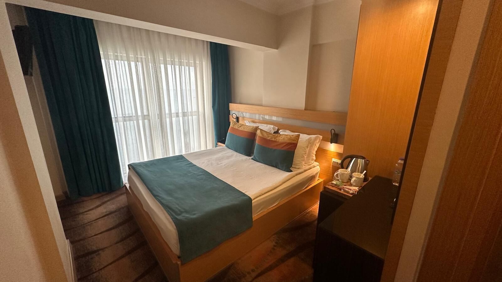 A hotel room with a bed, a nightstand, a coffee maker, and a window with curtains.