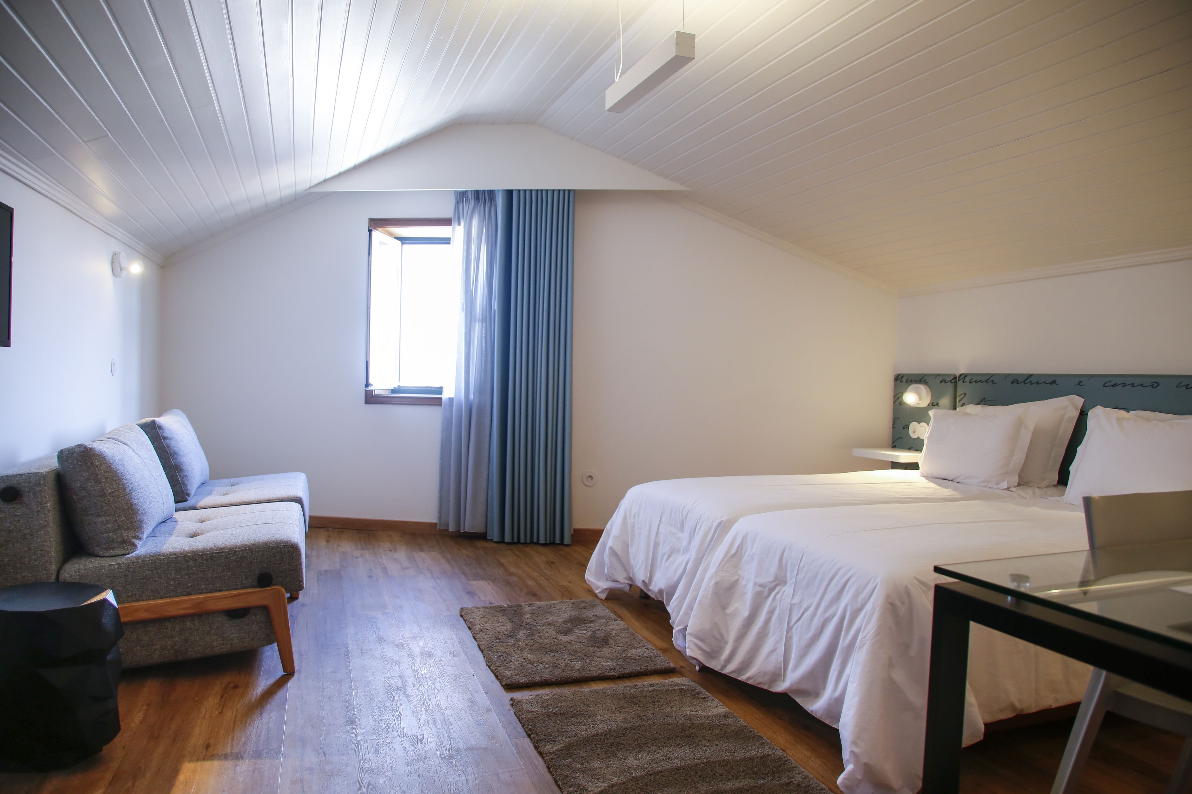 A bedroom with a bed, a desk, a sofa, and a window with curtains.