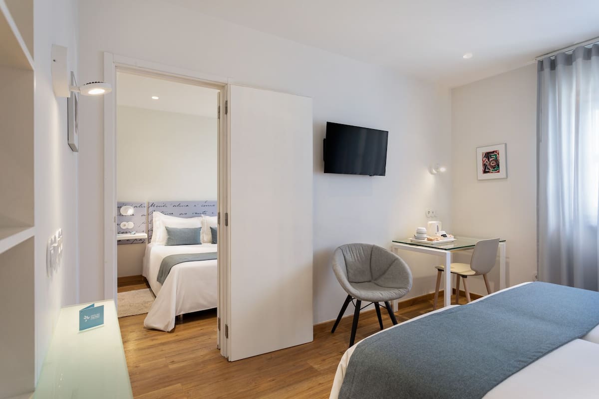 A hotel room with a bed, a desk, a chair, a TV, and a window with curtains.