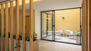 Un interior moderno con un separador de madera, suelo de baldosas y vistas a un comedor con sillas y mesas blancas.