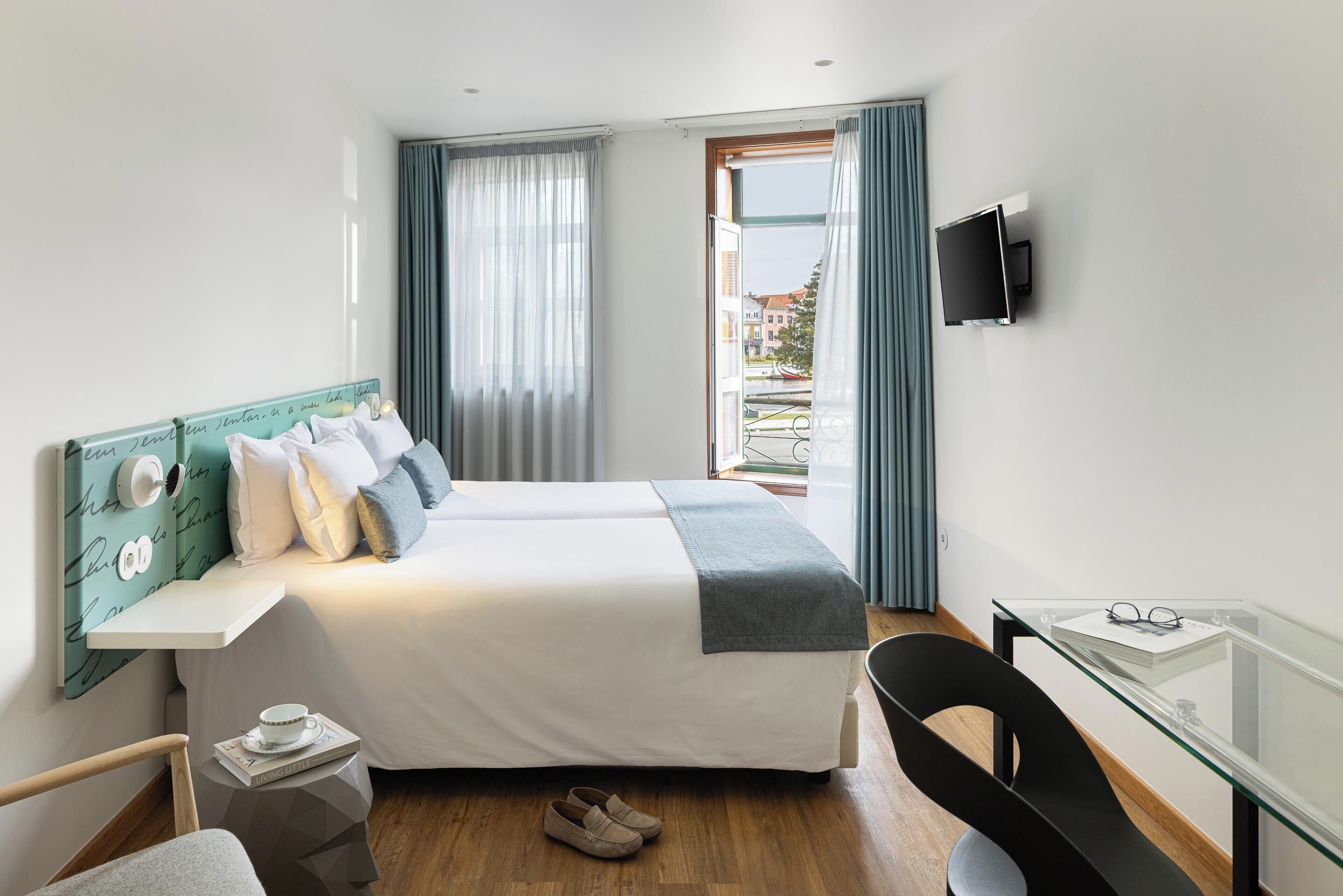 A hotel room with a bed, a desk, a chair, a TV, and a window with curtains.