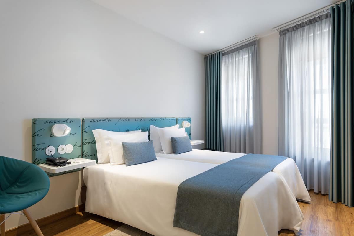 A hotel room with a bed, a desk with a phone, and a chair.