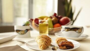 Une table mise pour le petit-déjeuner, avec des croissants, un panier de fruits et une tasse de thé.