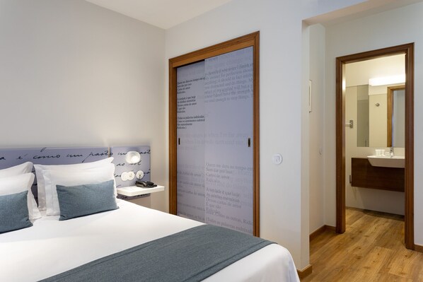 A bedroom with a bed, bedside table, and a large mirror in the adjacent bathroom. - Hotel das Salinas (Aveiro)