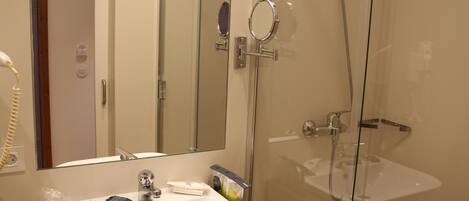 A bathroom with a glass-enclosed shower, a sink with a mirror, and toiletries on the counter.
