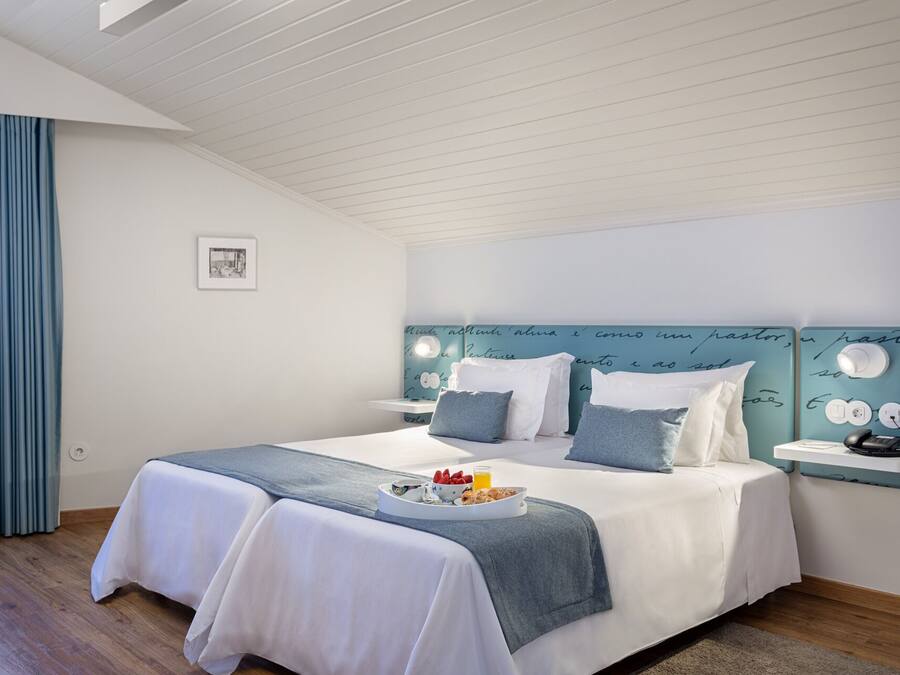 A bedroom with a bed, bedside tables, a headboard with writing, a picture on the wall, and a window with curtains.