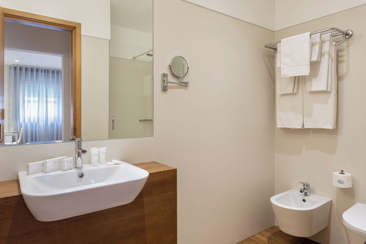 A bathroom with a sink, bidet, mirror, and towel rack.