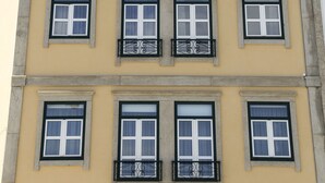 Un edificio con fachada amarilla, múltiples ventanas de marco negro y una cornisa decorativa.
