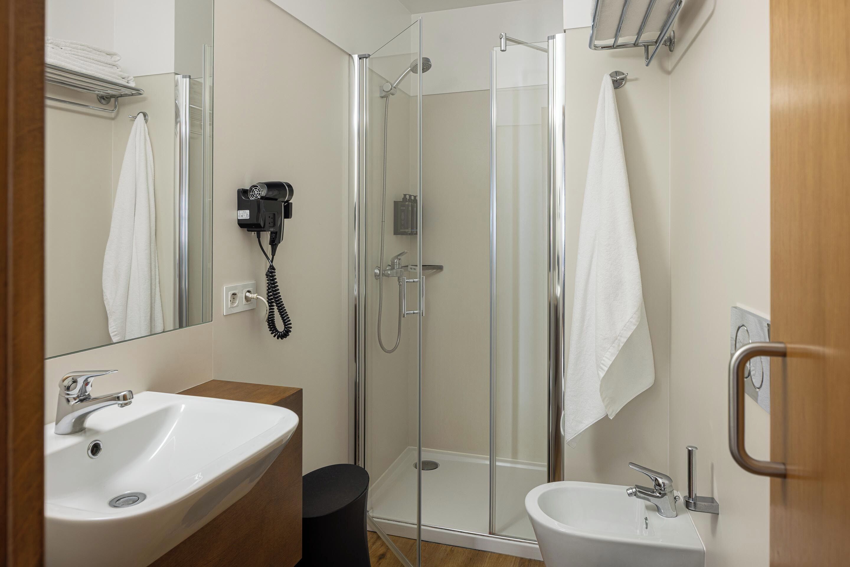 A bathroom with a glass shower enclosure, a sink, a bidet, and a towel rack.