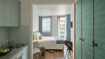 Une chambre à coucher avec un lit, une chaise, une petite table et une fenêtre avec des rideaux.