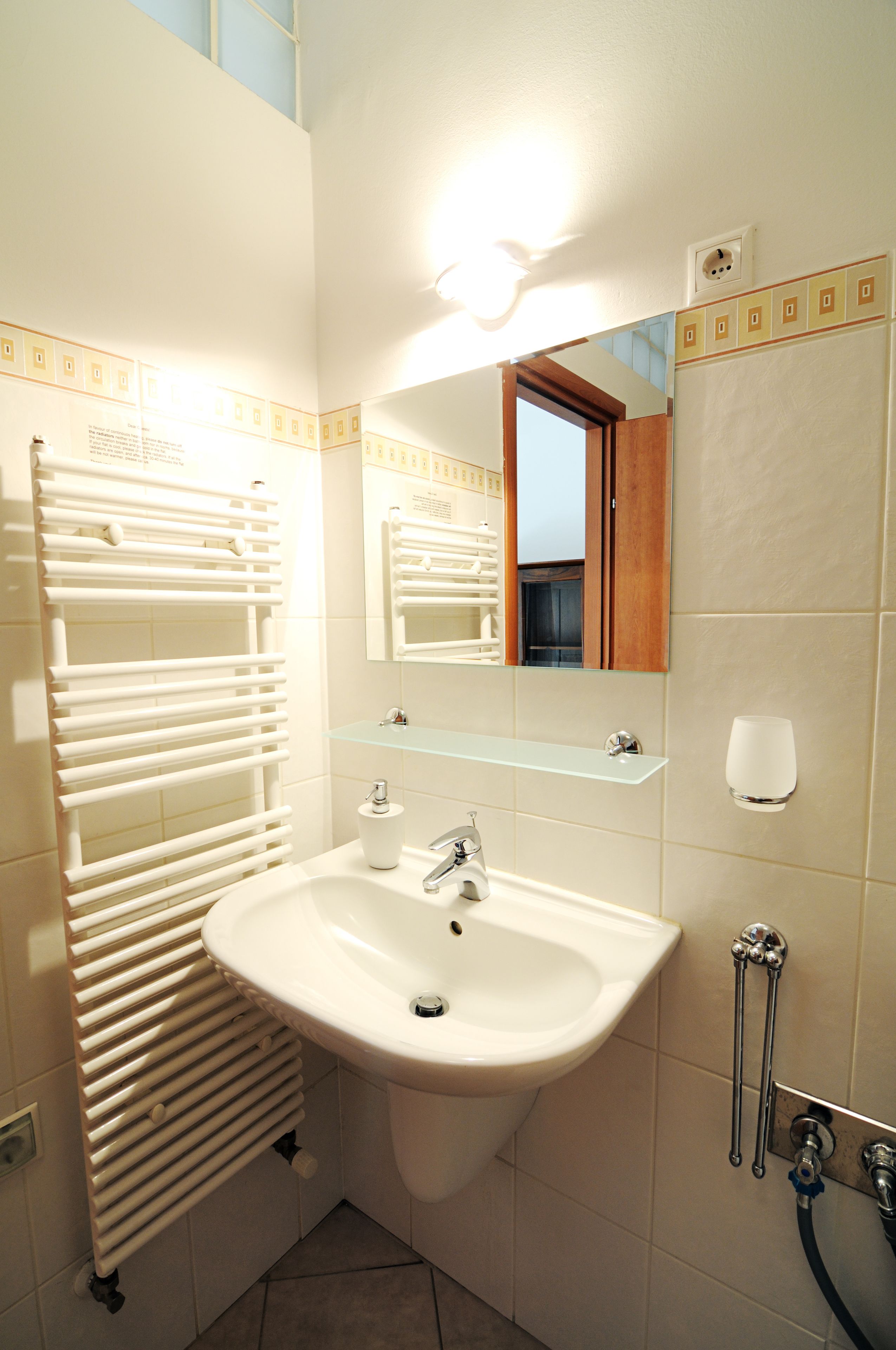 A bathroom with a white sink, mirror, towel rack, and a glass shelf.