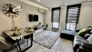 A modern living room with a dining area, a large wall clock, and a flat-screen TV. - Comfort Apartments (Budapest)