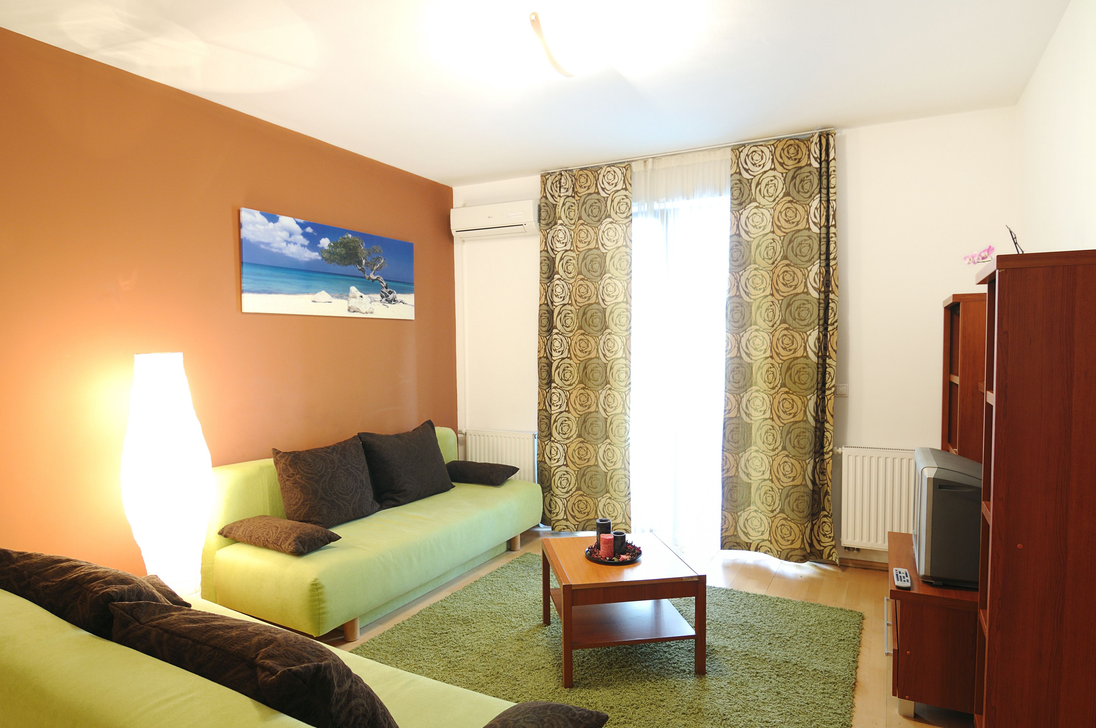 A living room with a green sofa, a wooden coffee table, and a television on a wooden stand.