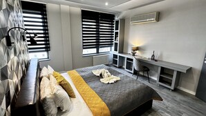 A modern bedroom with a large bed, a desk, and a window with blinds. - Comfort Apartments (Budapest)