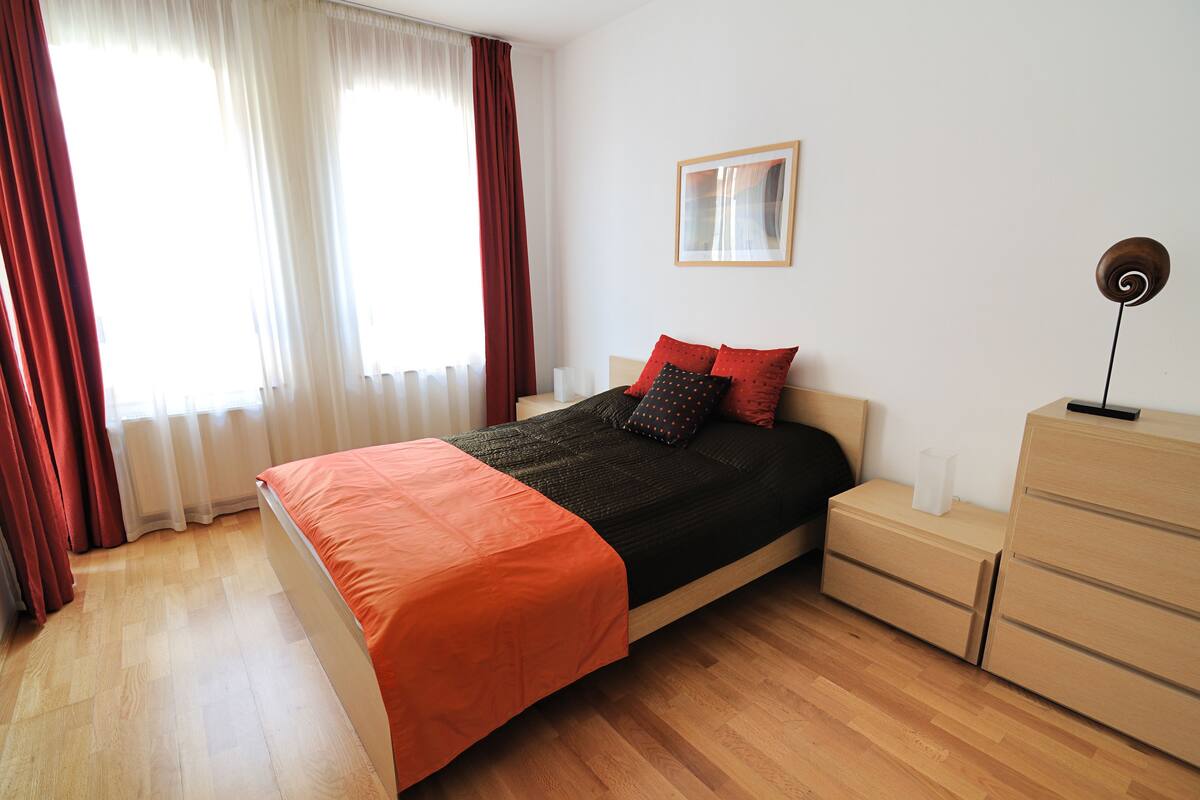 Un dormitorio con cama, mesita de noche, cómoda y ventana con cortinas.