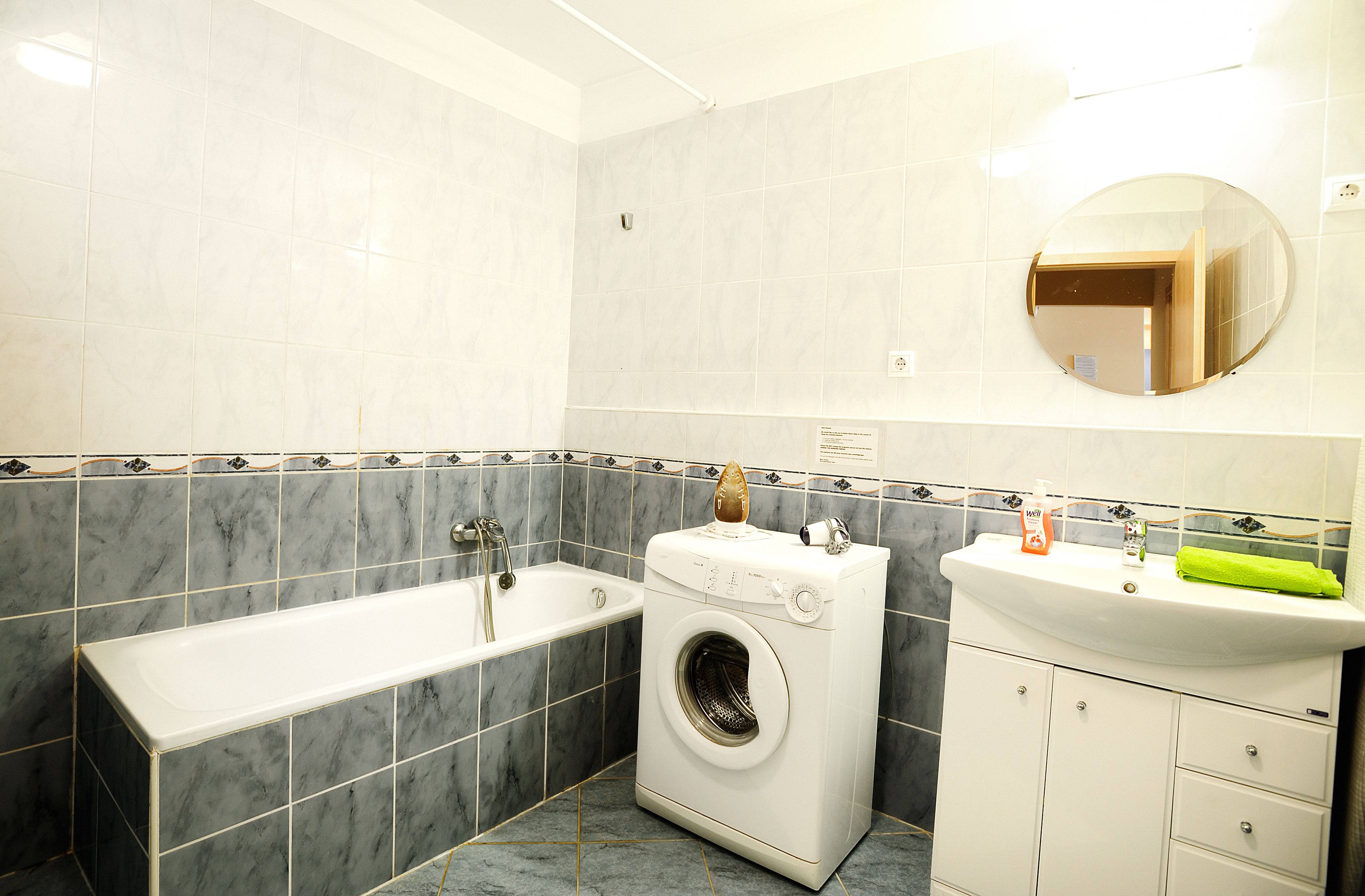A bathroom with a bathtub, a washing machine, and a sink with a mirror above it.