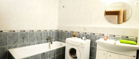 A bathroom with a bathtub, a washing machine, and a sink with a mirror above it.